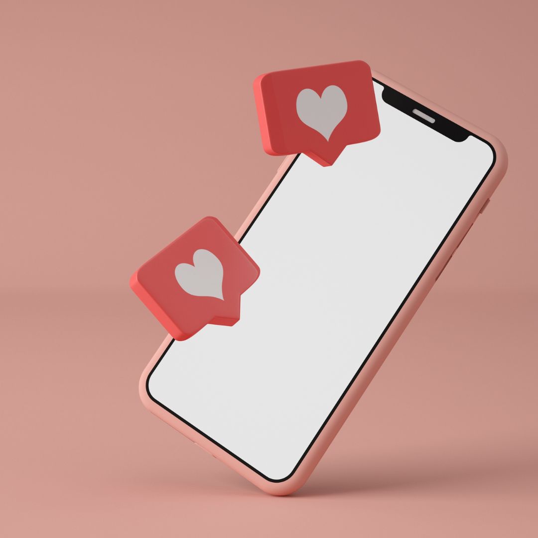 A modern smartphone with a blank white screen is tilted against a pink background, with floating red speech bubbles containing white heart icons representing social media likes.