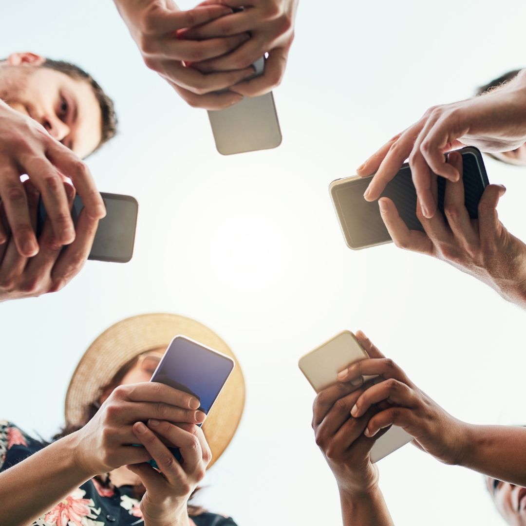 Circle of hands holding smartphones towards the sky