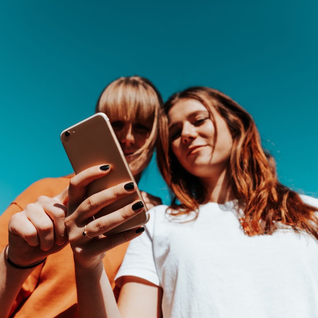 Two women outside looking at phone under blue sky