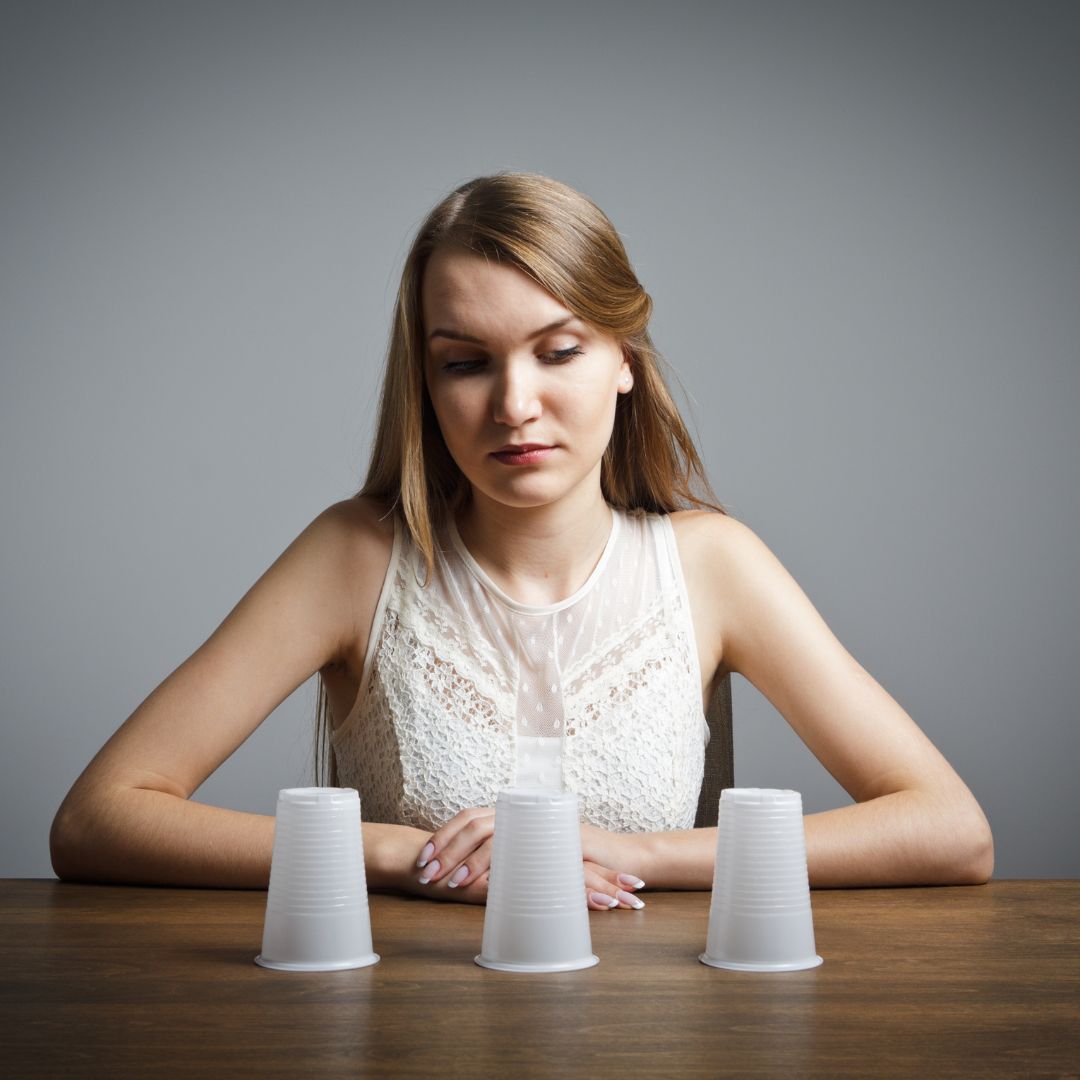 Woman staring at plastic cups on table in decision pose