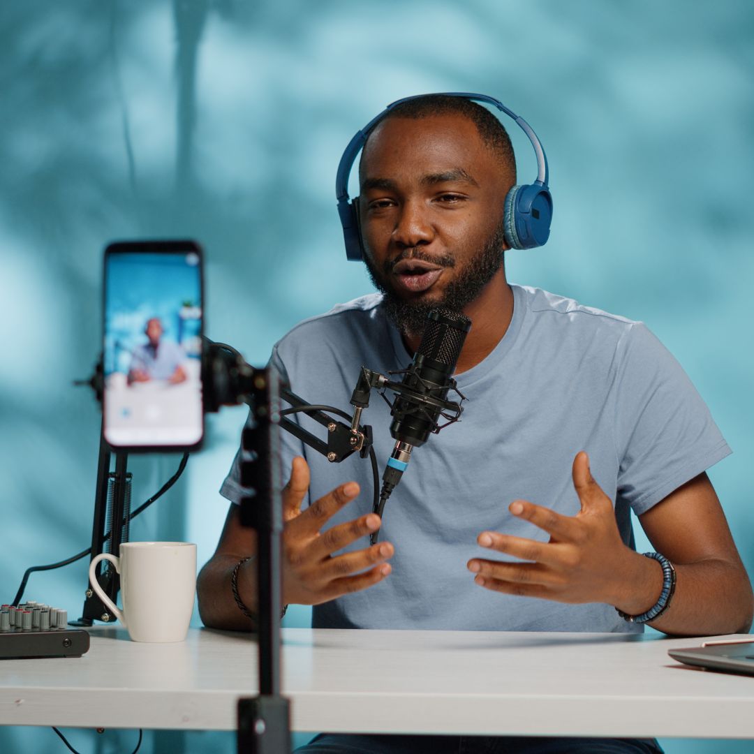 Man wearing headphones filming video content in a home studio setup with microphone, camera phone, and laptop representing content creation for pet brands.
