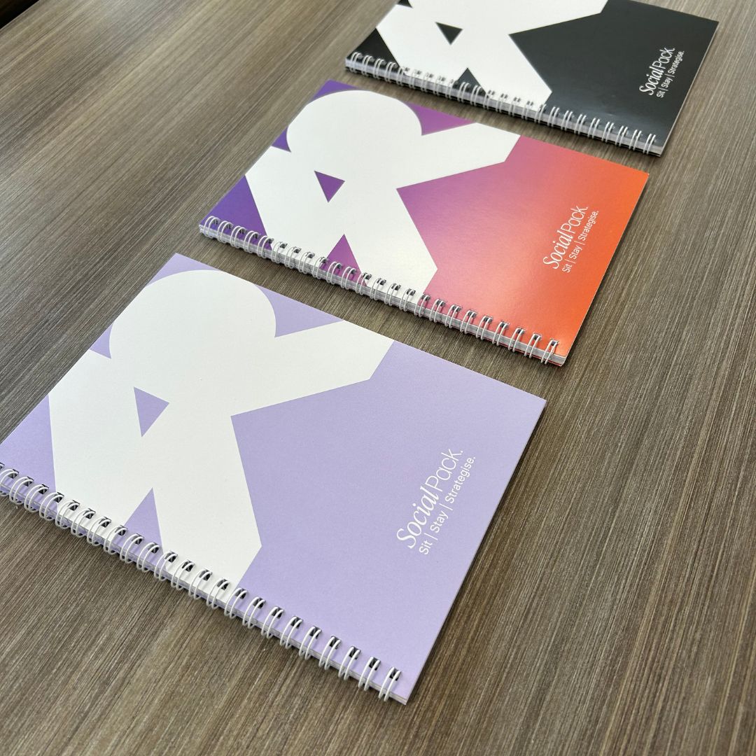 Three spiral-bound notebooks with colorful covers on a wooden surface